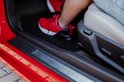 Personne en chaussures rouges monte dans une voiture avec tapis de sol noir.