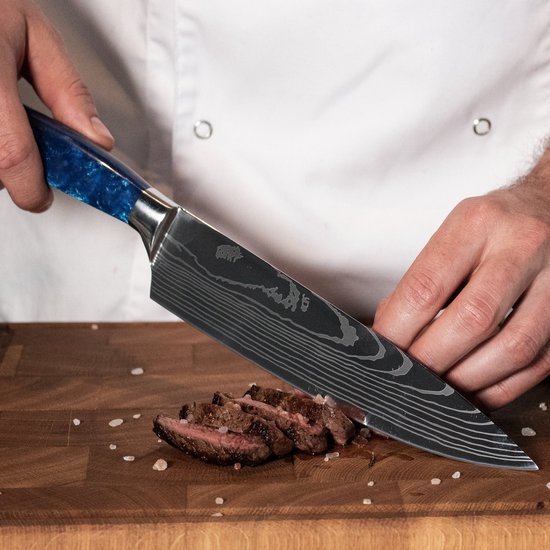 Een chefmes met damascusprint en blauw epoxy handvat snijdt gesneden biefstuk op een houten snijplank.