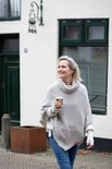 Vrouw met een lichtgrijze gebreide poncho met col, jeans en gebreide polswarmers.
