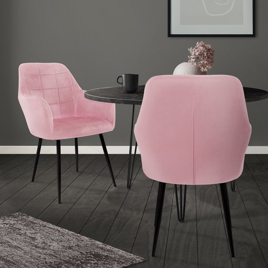 Deux chaises de salle à manger roses en velours avec accoudoirs, placées près d'une table ronde dans un salon.