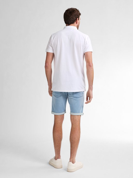 De achterkant van een witte polo met een klein logo op de linkerborst, gedragen door een man met een lichte spijkerbroek.