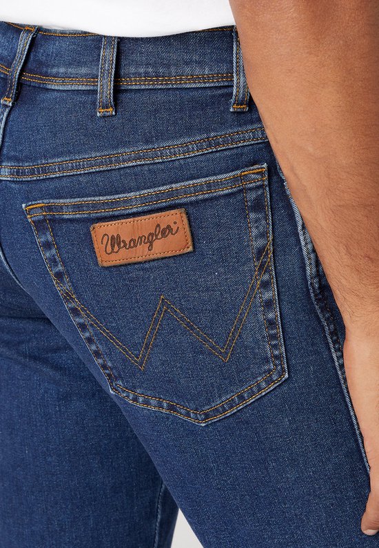 Close-up van de achterzak van een donkerblauwe Wrangler jeans met bruin lederen label.