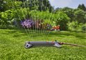 Grijze zwenksproeier met oranje onderdelen, water sproeiend op groen gras.