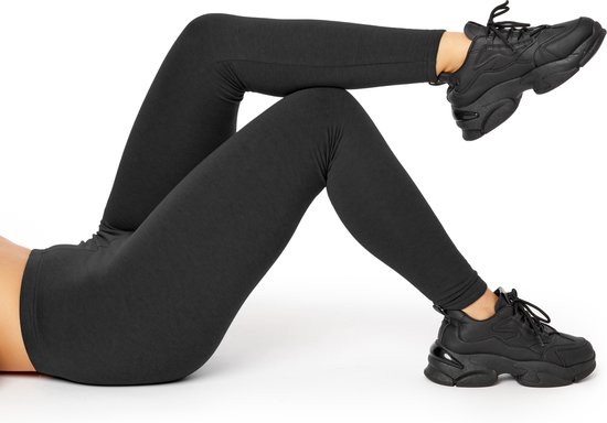 Gedetailleerd beeld van de benen van een vrouw in een donkere, nauwsluitende legging en zwarte sneakers, liggend op de grond.