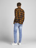 Man van achteren gezien in een lichtblauwe skinny jeans en een oranje met zwart geblokt overhemd.