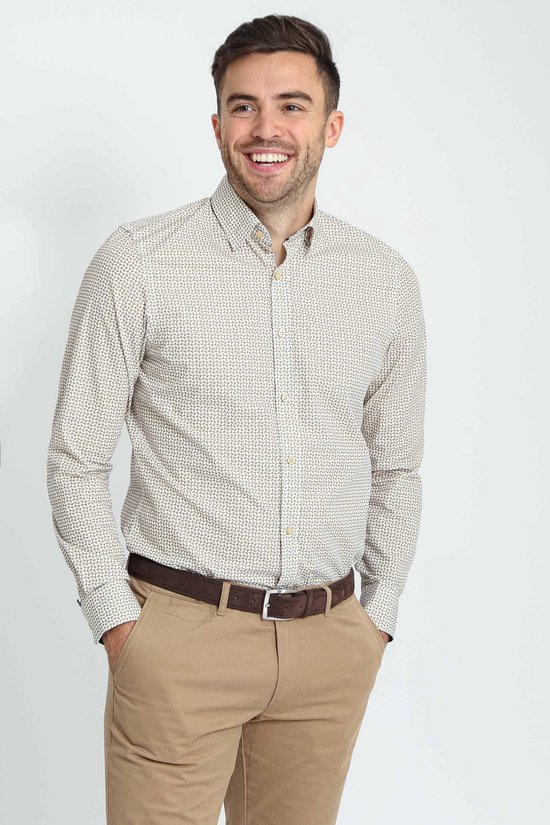 Man met de handen in de zakken, draagt een beige overhemd met een subtiel patroon en een bruine riem.
