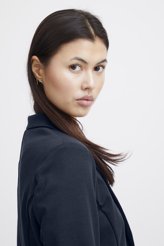 Model draait zich om, draagt een donkerblauwe blazer en kijkt over de schouder.