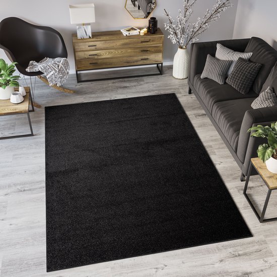Een antracietkleurig vloerkleed in een woonkamer, met een bank en stoel.