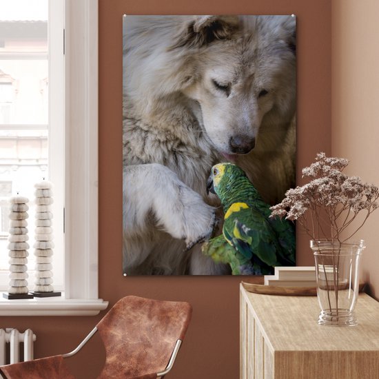 Een witte hond en een groene papegaai op een glasafbeelding aan een muur met een raam.