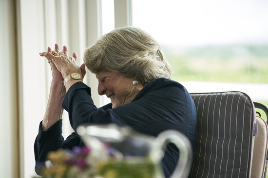 Dame Judi Dench, lachend met haar handen in elkaar gevouwen, met een gouden horloge om haar pols.