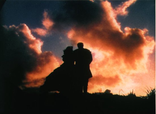 Silhouetten van een koppel tegen een dramatische zonsondergang met oranje wolken.