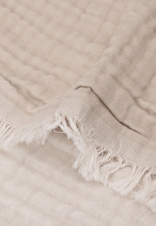 Detail van een lichtbruine mousseline deken met rafels en textuur.
