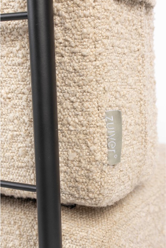 Close-up van de beige bouclé stof van een bank, met een zwart metalen frame en een 'Zuiver' logo.