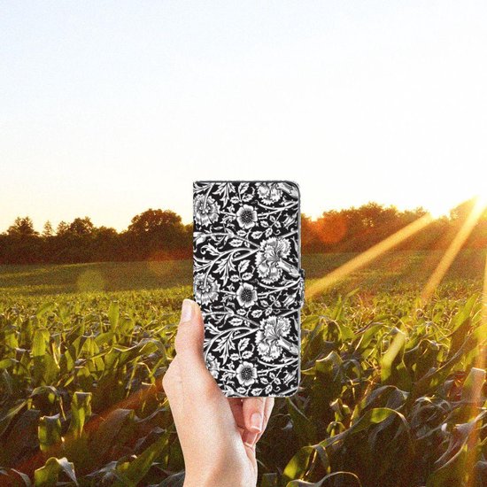 Een hand houdt een zwart telefoonhoesje met bloemenpatroon vast in een maïsveld.