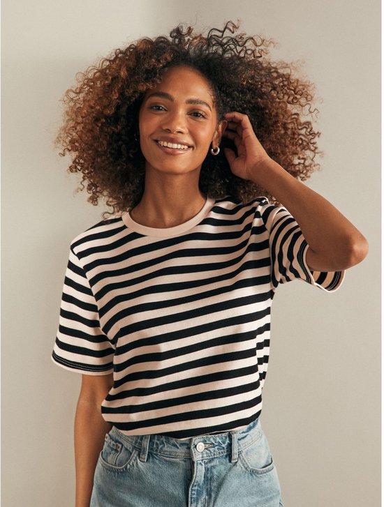 Lachende vrouw met krullend bruin haar draagt een gestreepte t-shirt met zwart-witte strepen.
