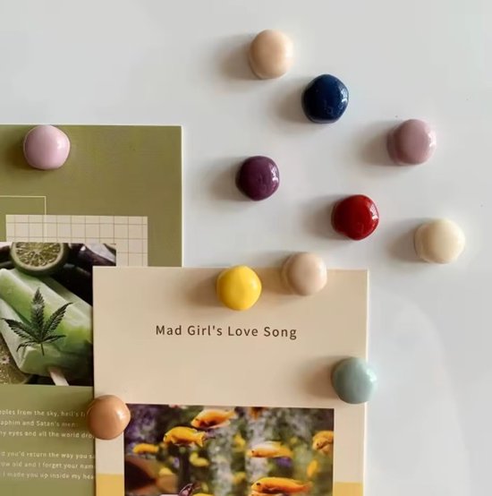 Een verzameling ronde, gekleurde magneten: lichtroze, donkerblauw, paars, rood, lichtgeel, beige en groen, op kaarten.