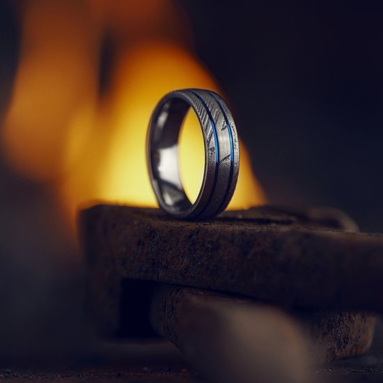 Een zilverkleurige ring met blauwe accenten, rustend op een metalen voorwerp bij vuur.