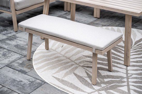 Lichte houten bank met grijze stoffen zitting op een rond vloerkleed met bladmotief.
