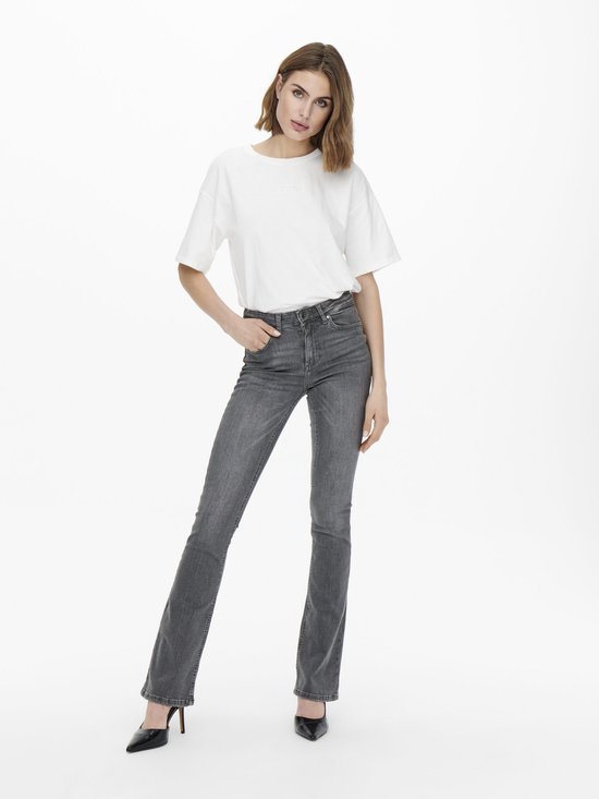 Model in een grijze spijkerbroek met flared pijpen en een witte top.
