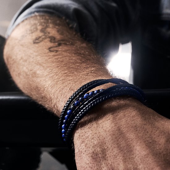 Close-up van een zwarte gevlochten leren armband met blauwe lapis lazuli kralen om een man's pols.