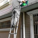 Man in grijze cargobroek staat op een ladder, met een groene gereedschapskist op de dakrand.