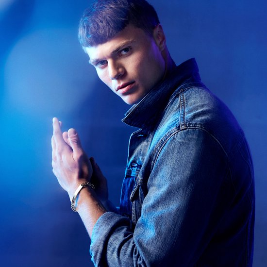 Jonge man met denim jack draagt zilverkleurige ID-plaatarmband om zijn pols.
