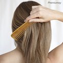 Een vrouw kamt haar bruine haar met een bamboe kam.