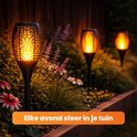 Drie zwarte tuin fakkels met vlam effect in een tuin met bloemen en struiken. Zorgt elke avond voor sfeer in je tuin.