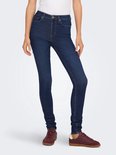 Een model draagt een donkerblauwe skinny jeans met hoge taille en bruine schoenen.