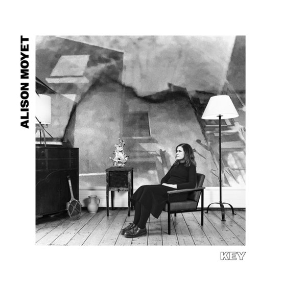 Alison Moyet, 'Key'. Een zwart-witfoto van een vrouw die in een stoel zit met een lamp en een kast.