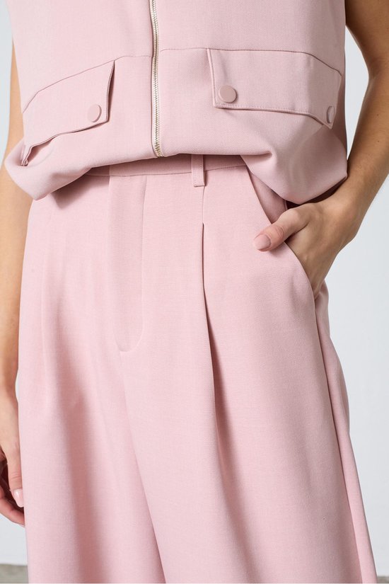 Detail van een lichtroze wijde broek met plooien, gedragen met een bijpassend topje.