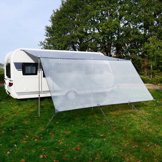 Grijze voorwand voor caravan luifel, opgezet op een grasveld naast een caravan.