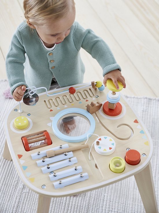 Een jong kind met een mintgroene trui speelt met een houten activiteitentafel met een xylofoon, spiegel en kralenbaan.