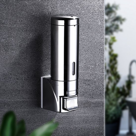 Zilverkleurige zeepdispenser aan de muur bevestigd met een drukknop, in een badkamer met planten.