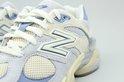 Detail van een New Balance sneaker met beige suède, mesh en lichtblauwe accenten, met witte veters.