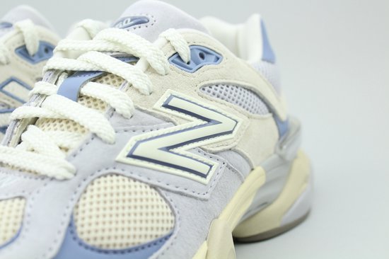 Detail van een New Balance sneaker met beige suède, mesh en lichtblauwe accenten, met witte veters.