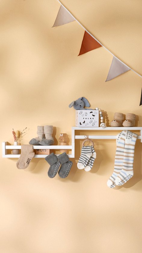 Verschillende babysokjes, slofjes en een pluchen konijn op een wandplank.