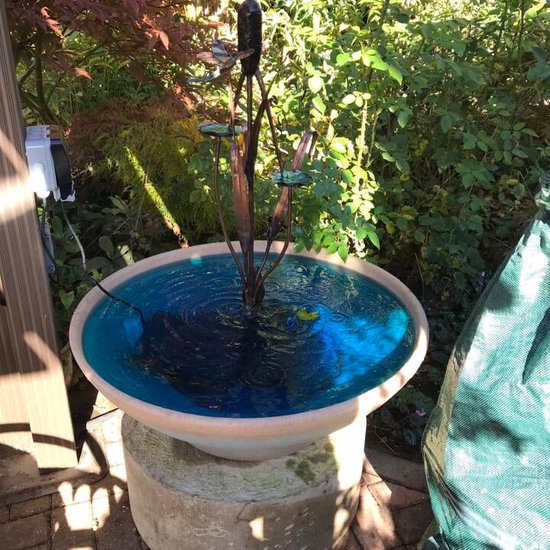 Terracotta fonteinbak op sokkel met helderblauwe vloeistof en een metalen waterornament.