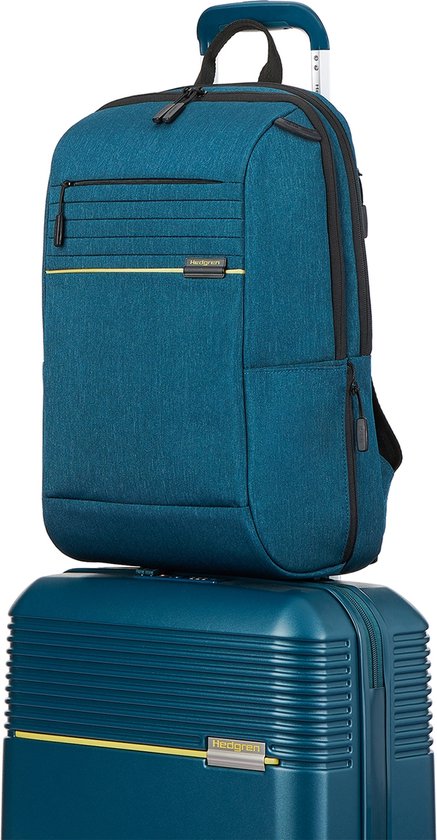Blauwe Hedgren rugzak met een gele accentlijn, bovenop een blauwe koffer.