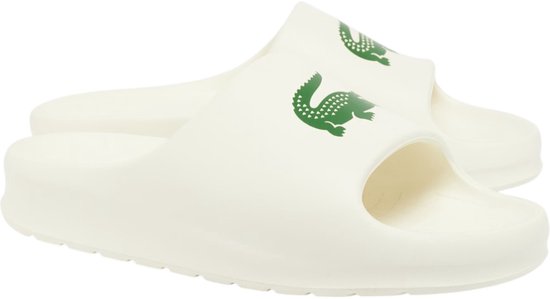 Crèmekleurige Lacoste slipper met groen krokodillenlogo op de band. Twee slippers zichtbaar.