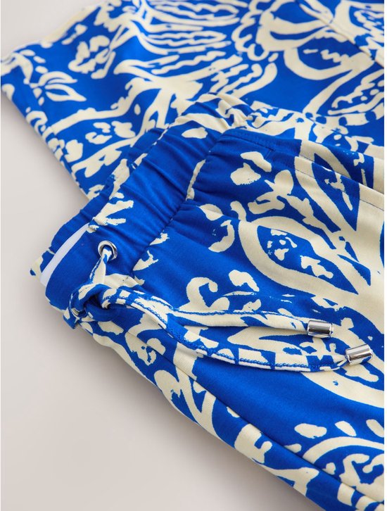 Detail van de tailleband en zak van een wijde broek met blauwe en crème paisley print.