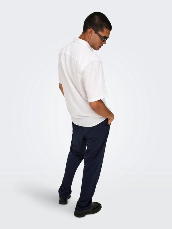 Man met donkere broek en wit hemd, handen in zakken.