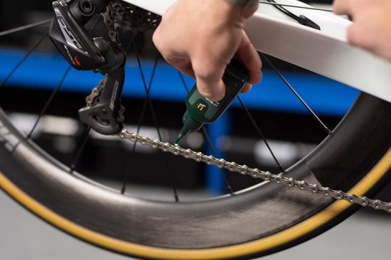 Hand die fles kettingolie boven fietsketting houdt. Druppelt groene olie op de ketting.