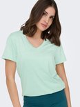 Lichtgroen V-hals t-shirt met korte mouwen, gedragen door een model met een turquoise broek.