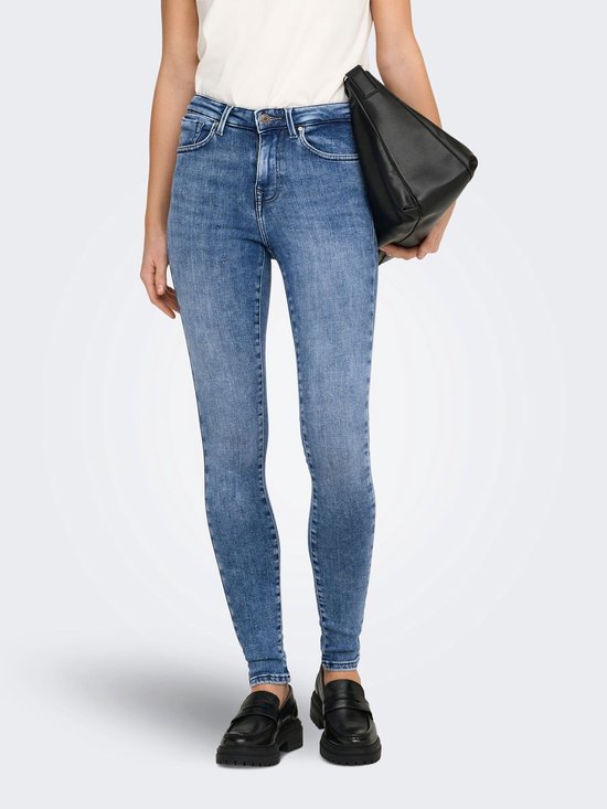 Model in blauwe skinny jeans met middelhoge taille, wit T-shirt en zwarte loafers.
