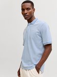 Man in lichtblauw poloshirt met witte kraag en manchetten, beige broek.