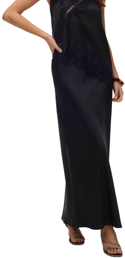 Gros plan d'une jupe longue noire en satin avec des détails en dentelle, portée avec des sandales à lanières.