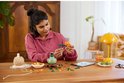 Une femme assise à une table construit un chrysanthème Lego. Les fleurs sont orange et rouges.