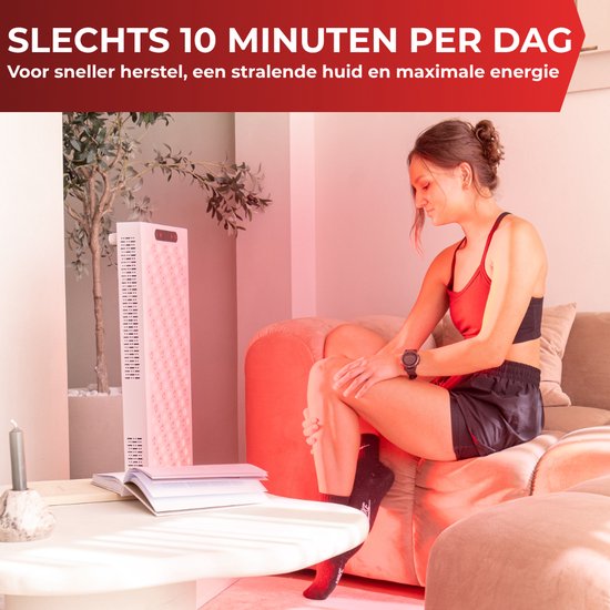 Vrouw zit op een bank en houdt haar been vast, terwijl ze voor een rood lichttherapiepaneel zit.