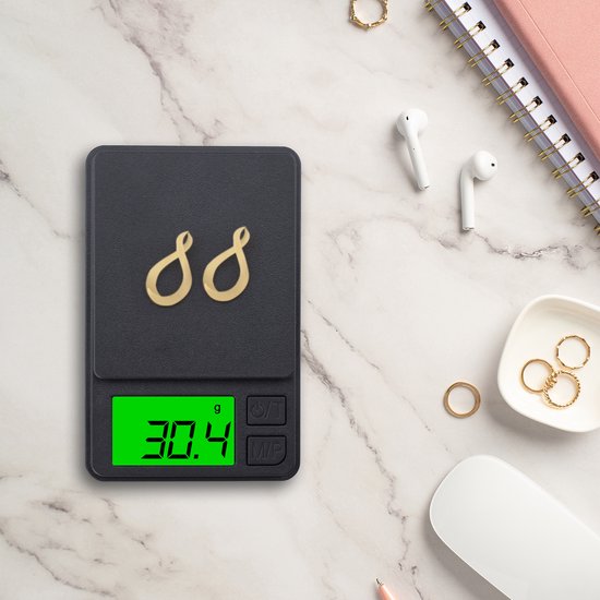 Gouden oorhangers in de vorm van het oneindigheidssymbool op een zwarte digitale weegschaal die 30.4 gram aangeeft.